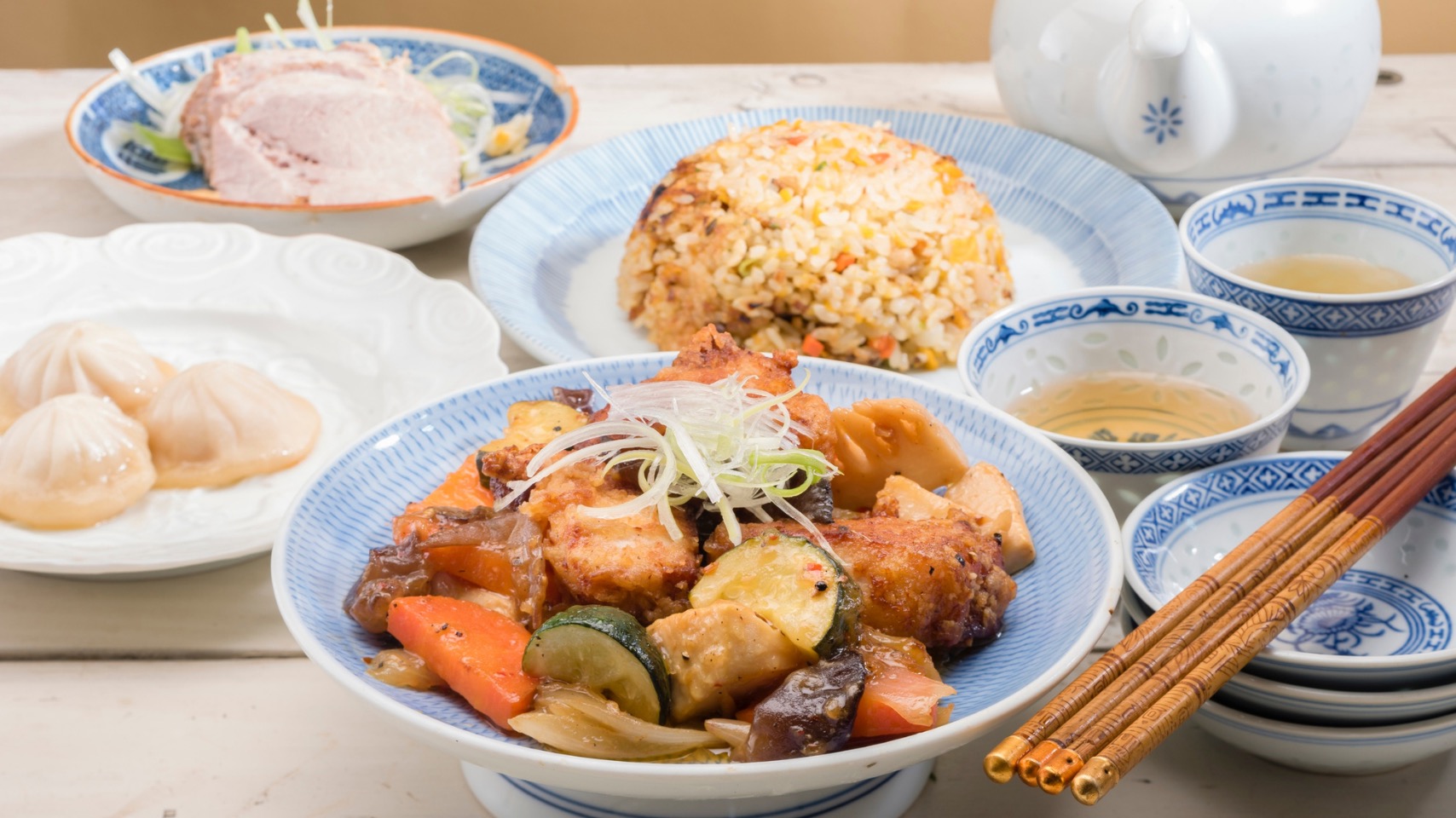 Preparat asiatic servit alături de orez, legume și ceai, într-o compoziție care ilustrează structura unei mese echilibrate.